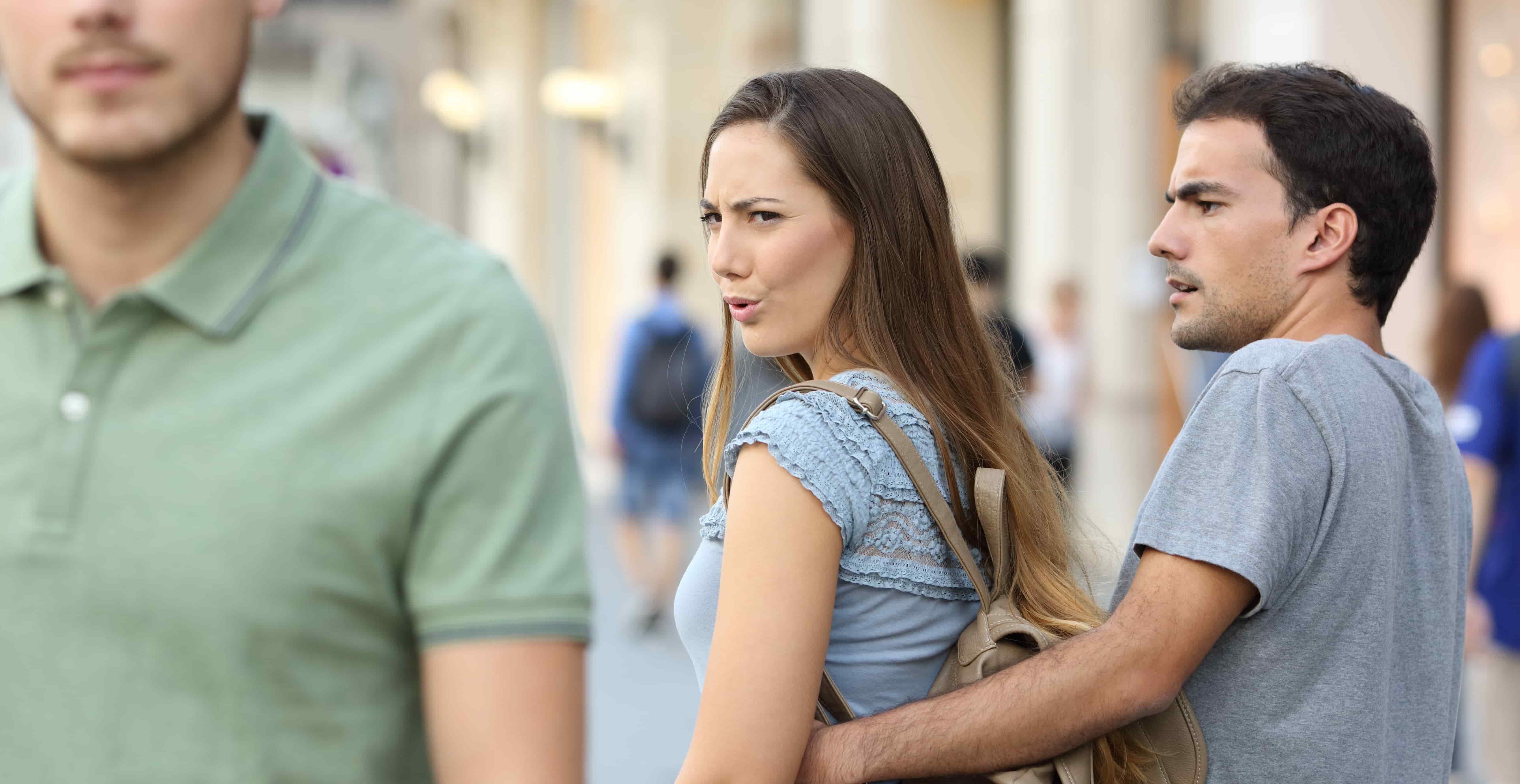 Disloyal woman looking another man and her angry boyfriend looking at her on the street
